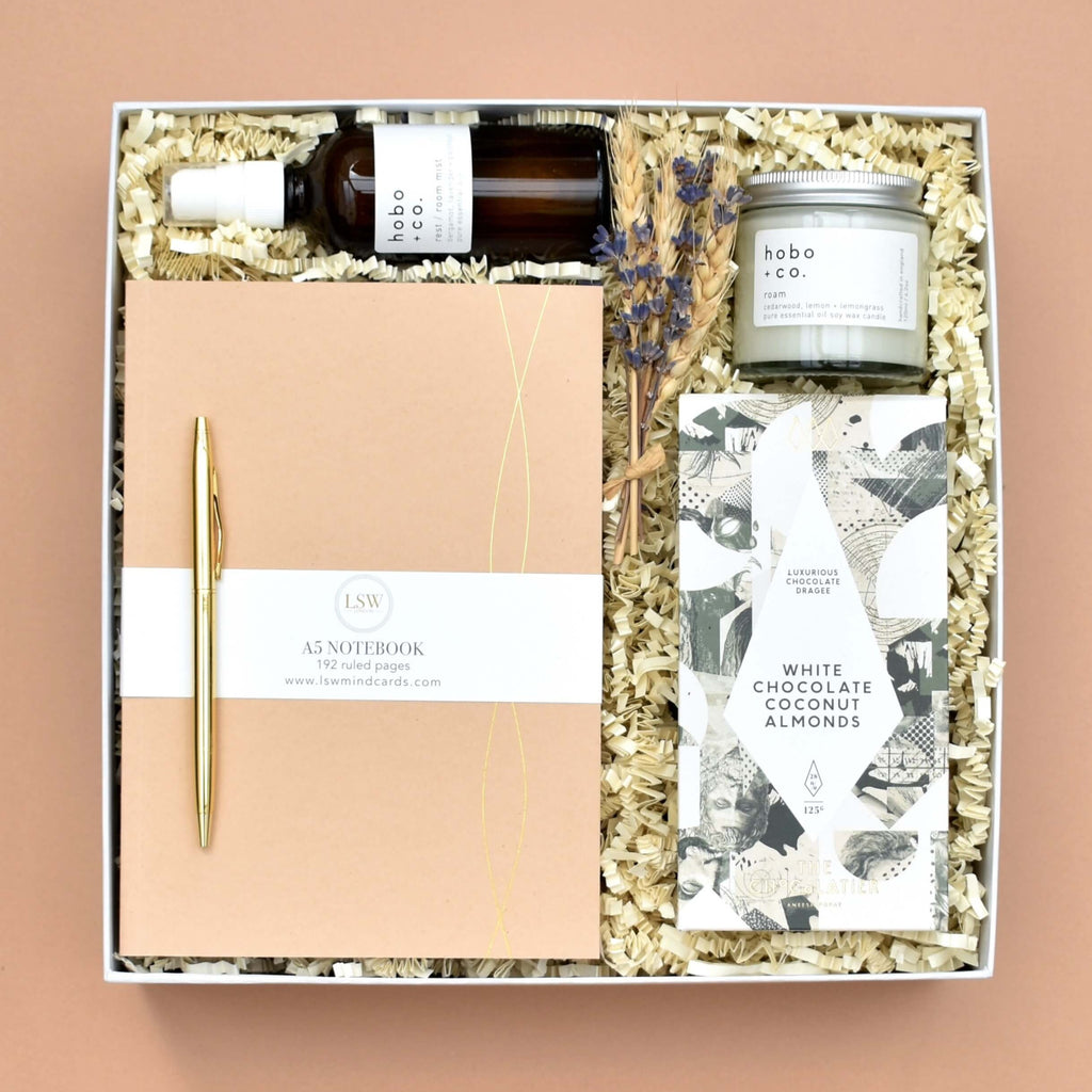 scandinavian luxury british gift box featuring small independent businesses. includes A5 notebook, gold pen, The Chocolatier almonds, hoco and co roam soy wax candle, and hobo and co room mist in rest. gift for her, employee gift